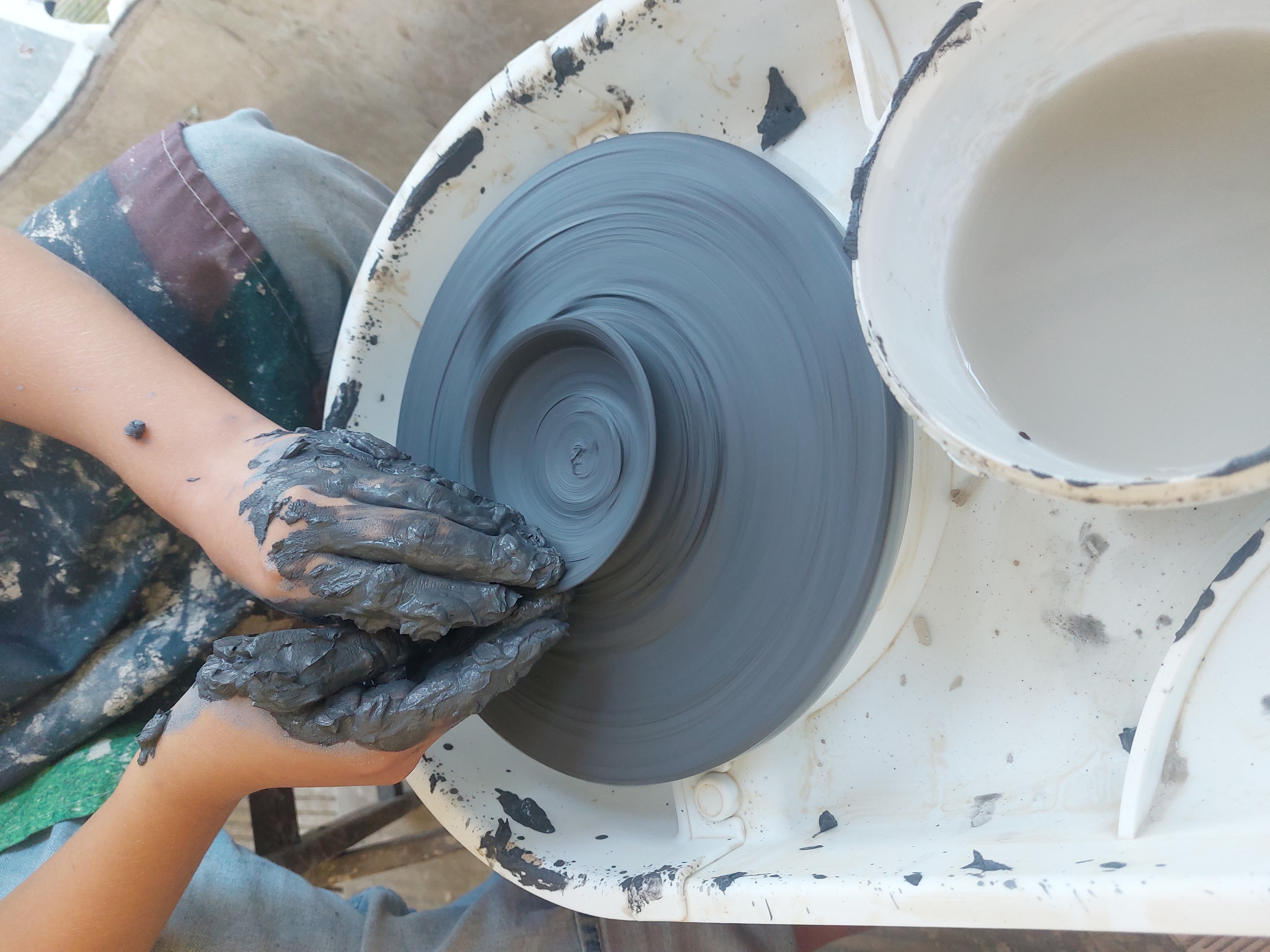 Hands form clay on a potter's wheel.