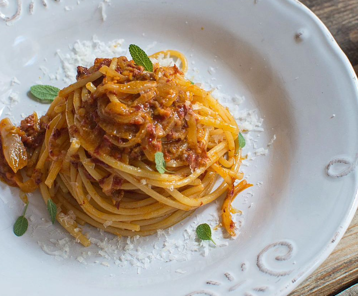 Spaghetti on a plate surrounded by sauce and herbs.
