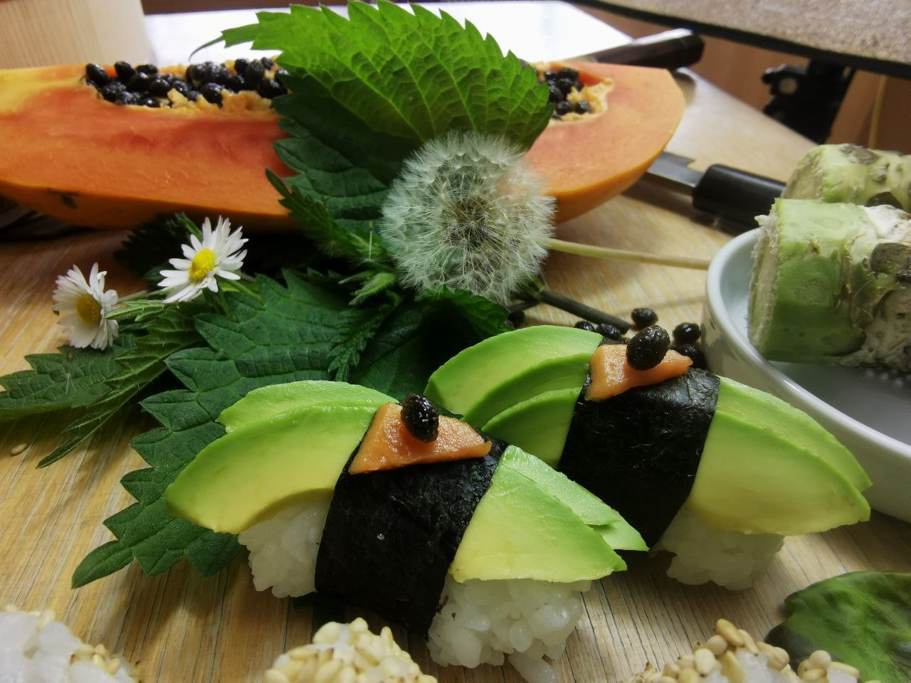 Sushi mit Avocado, umgeben von frischen Kräutern und Früchten.