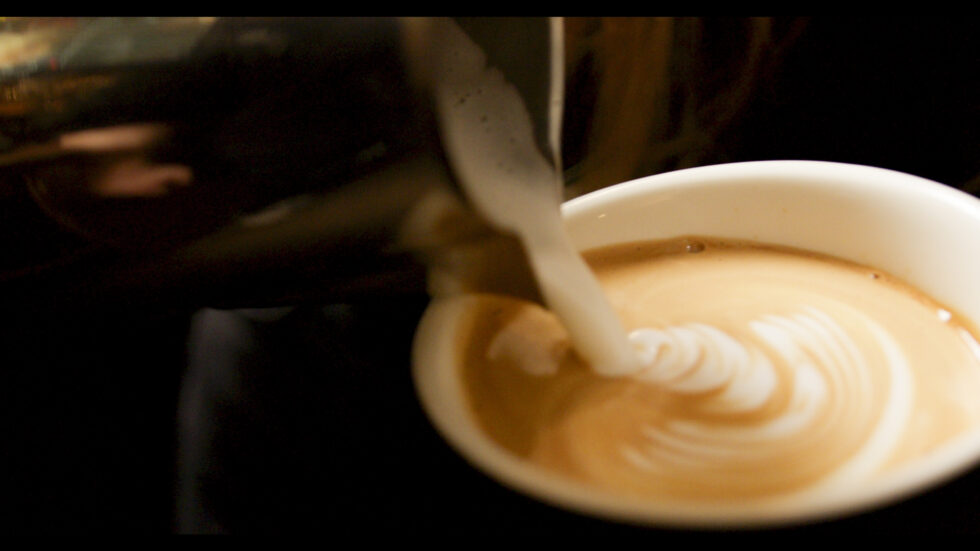 Milch wird in eine Kaffeetasse gegossen; gemütliche Atmosphäre.