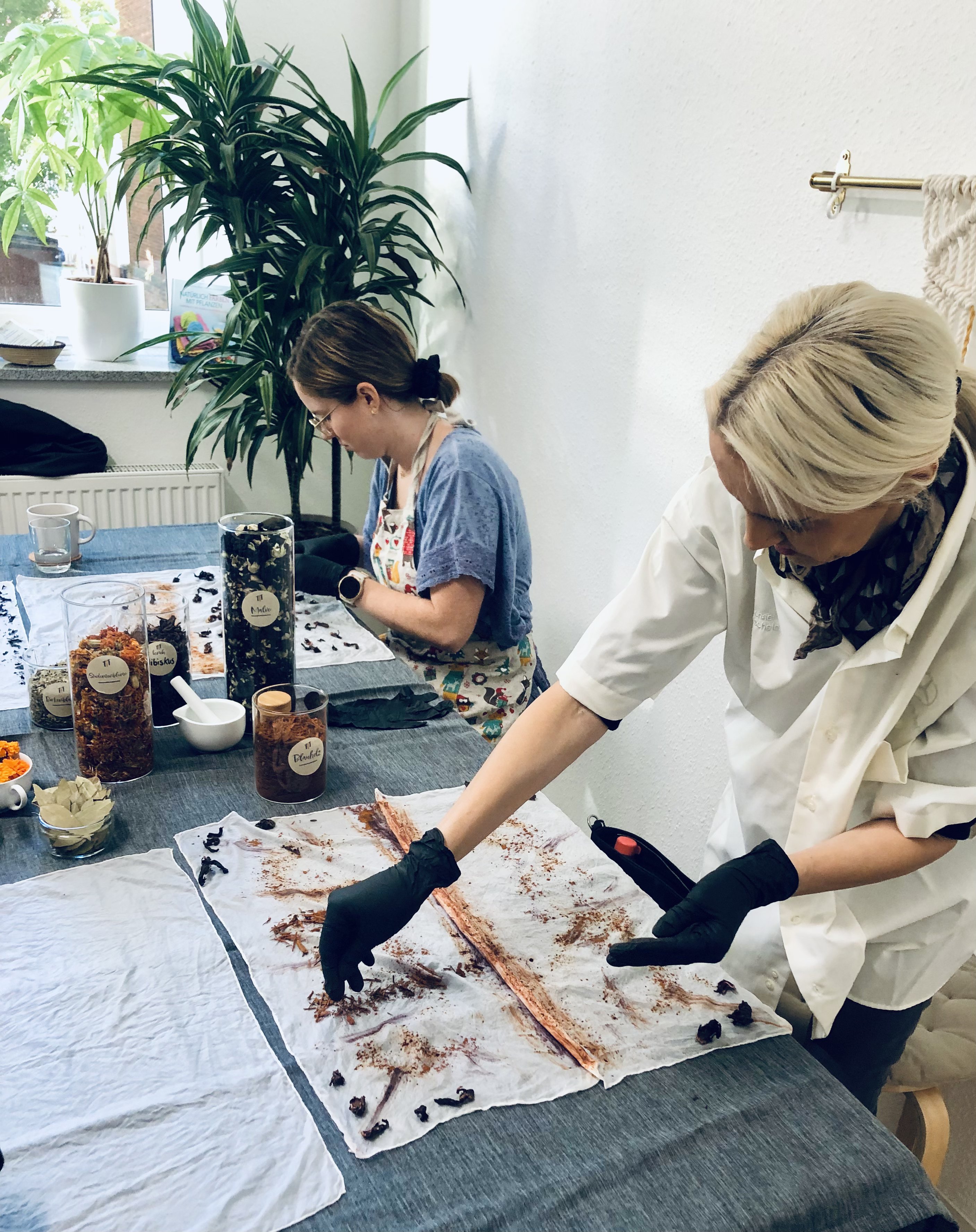 Frau platziert Naturmaterialien auf Seidentuch während Workshop im Raum.