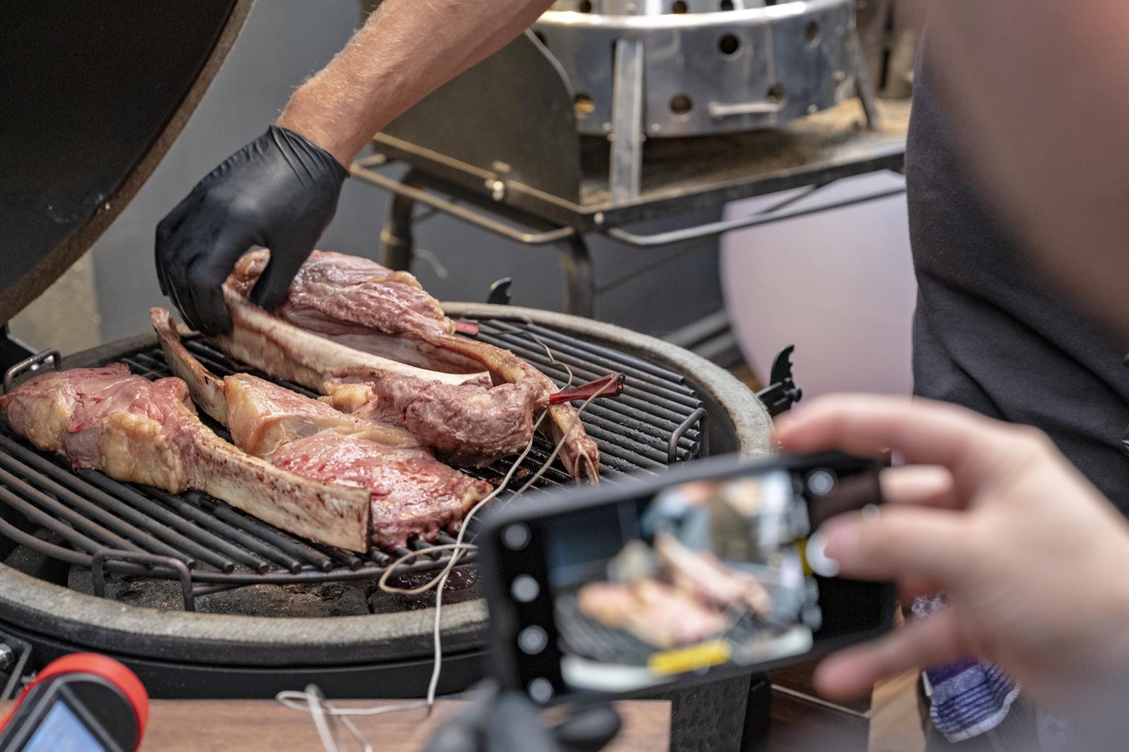 Fleisch wird grilliert, während jemand ein Foto macht.