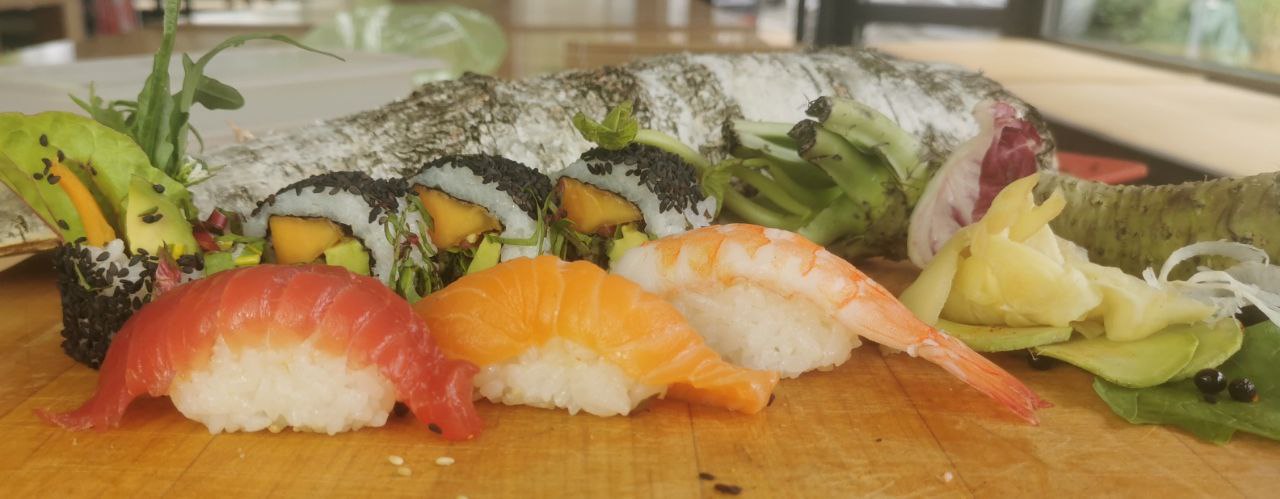 Sushi wird auf einem Holzbrett serviert, umgeben von frischen Zutaten.