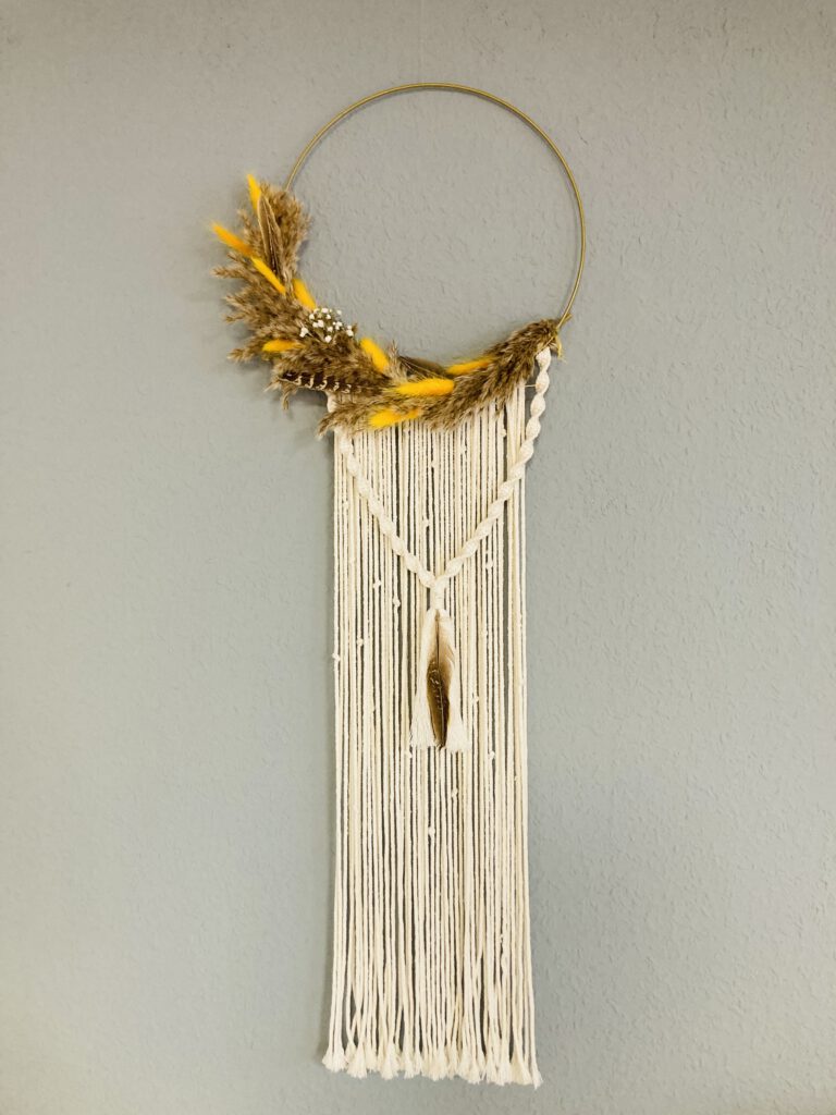 Wanddekoration mit natürlichen Materialien hängt an grauer Wand.