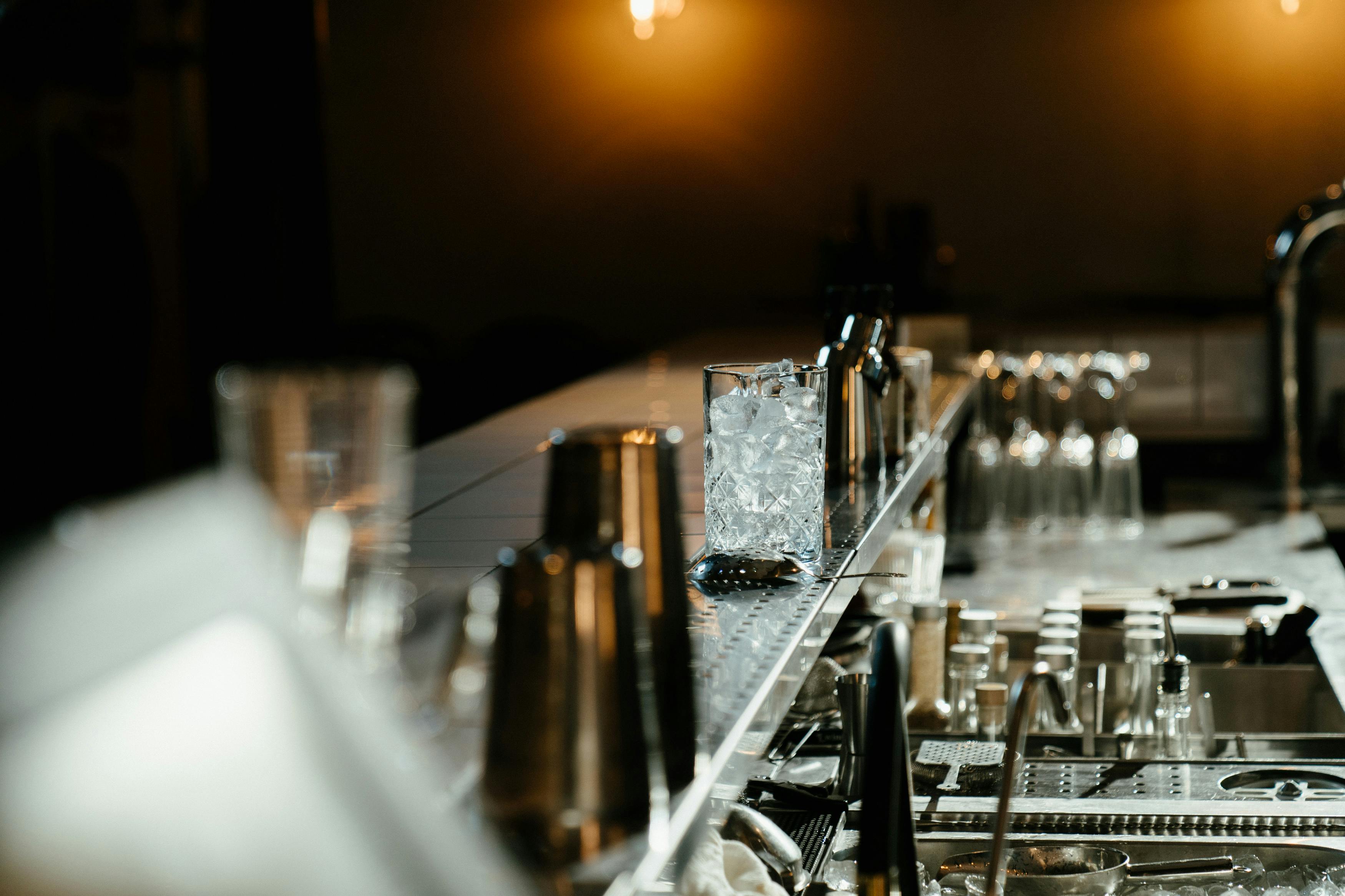Glas mit Eis steht auf einer Bar, umgeben von Gläsern.