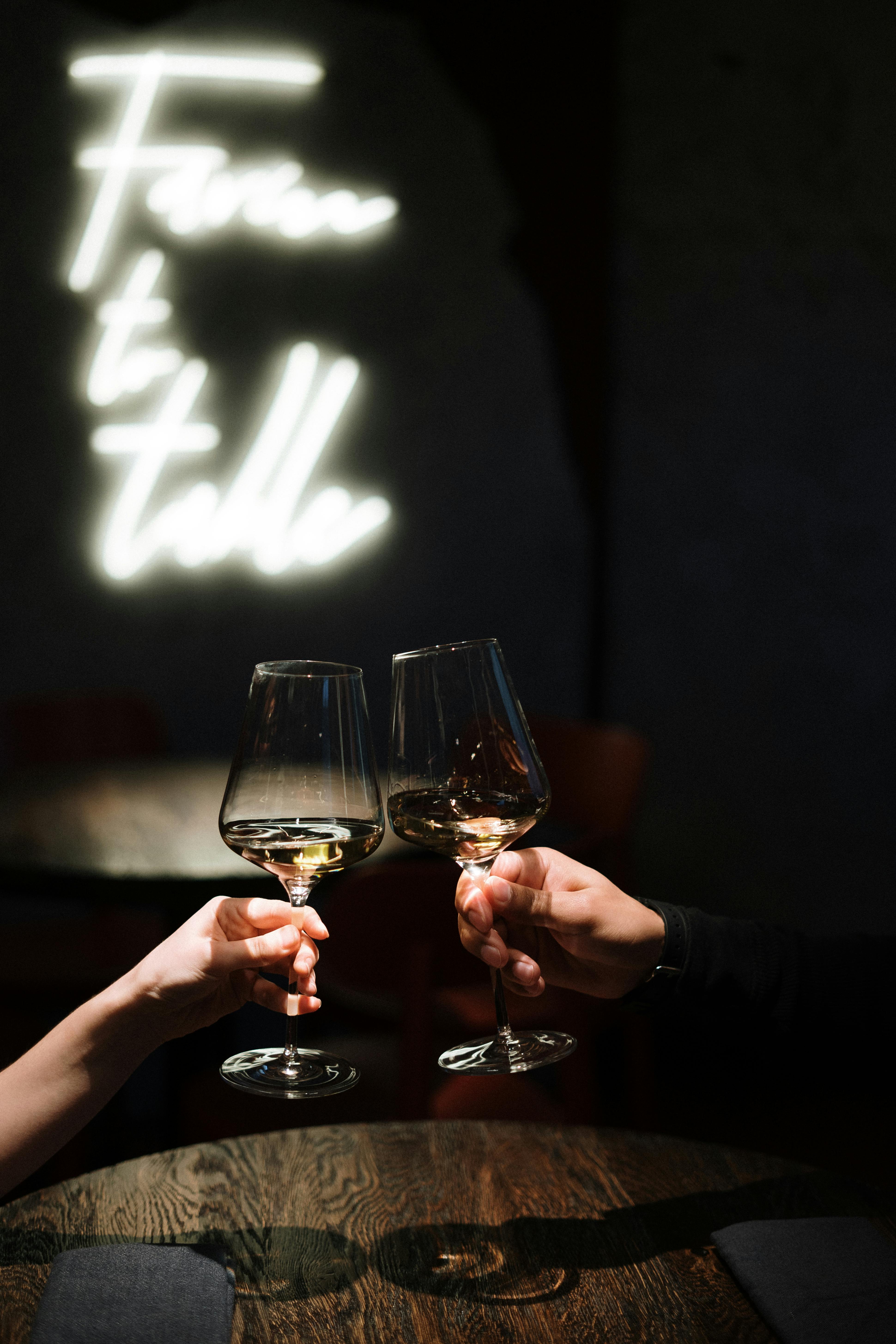 Two wine glasses are held to toast, dark background.
