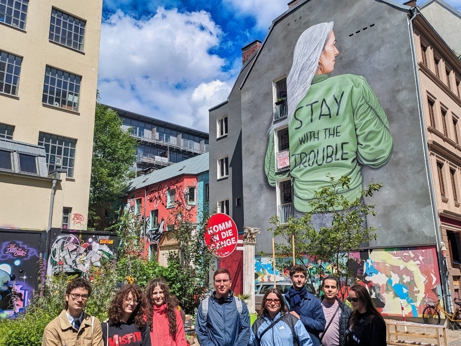 Group stands in front of a wall painting with the inscription “STAY WITH THE TROUBLE.”