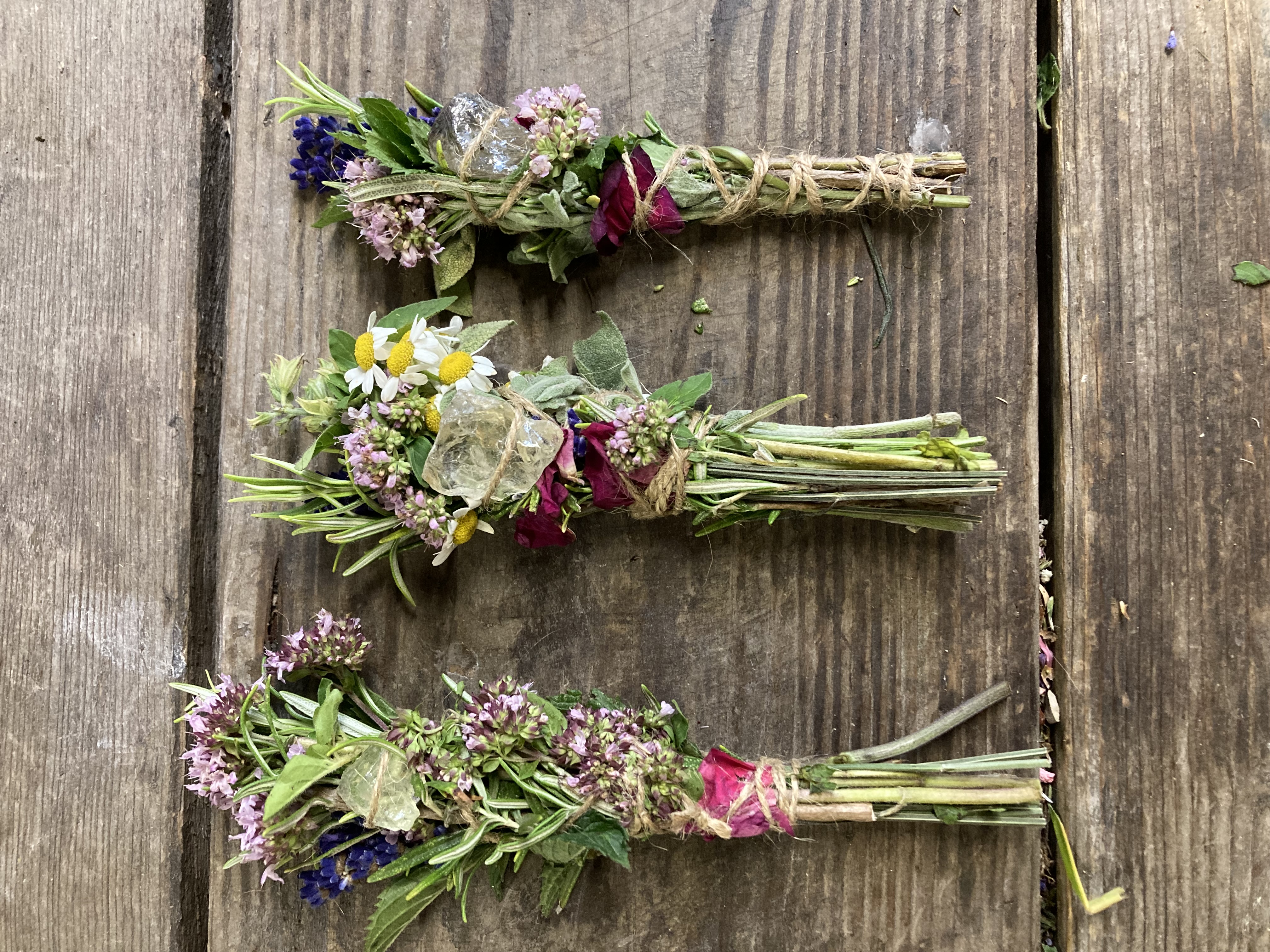 Drei Blumensträuße mit Kräutern und Kristallen auf Holz.