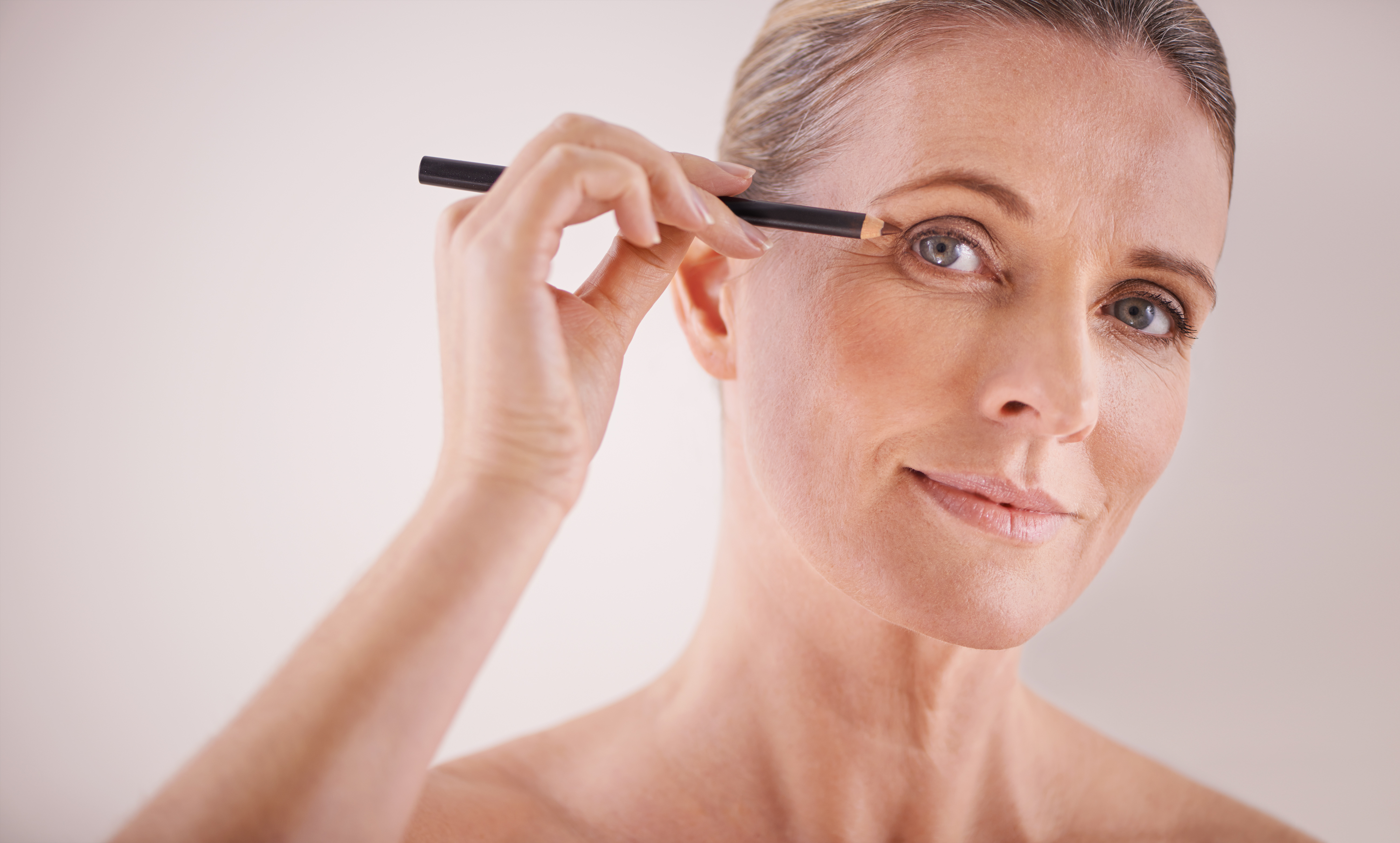 Frau schminkt sich mit einem Stift vor einem weißen Hintergrund.