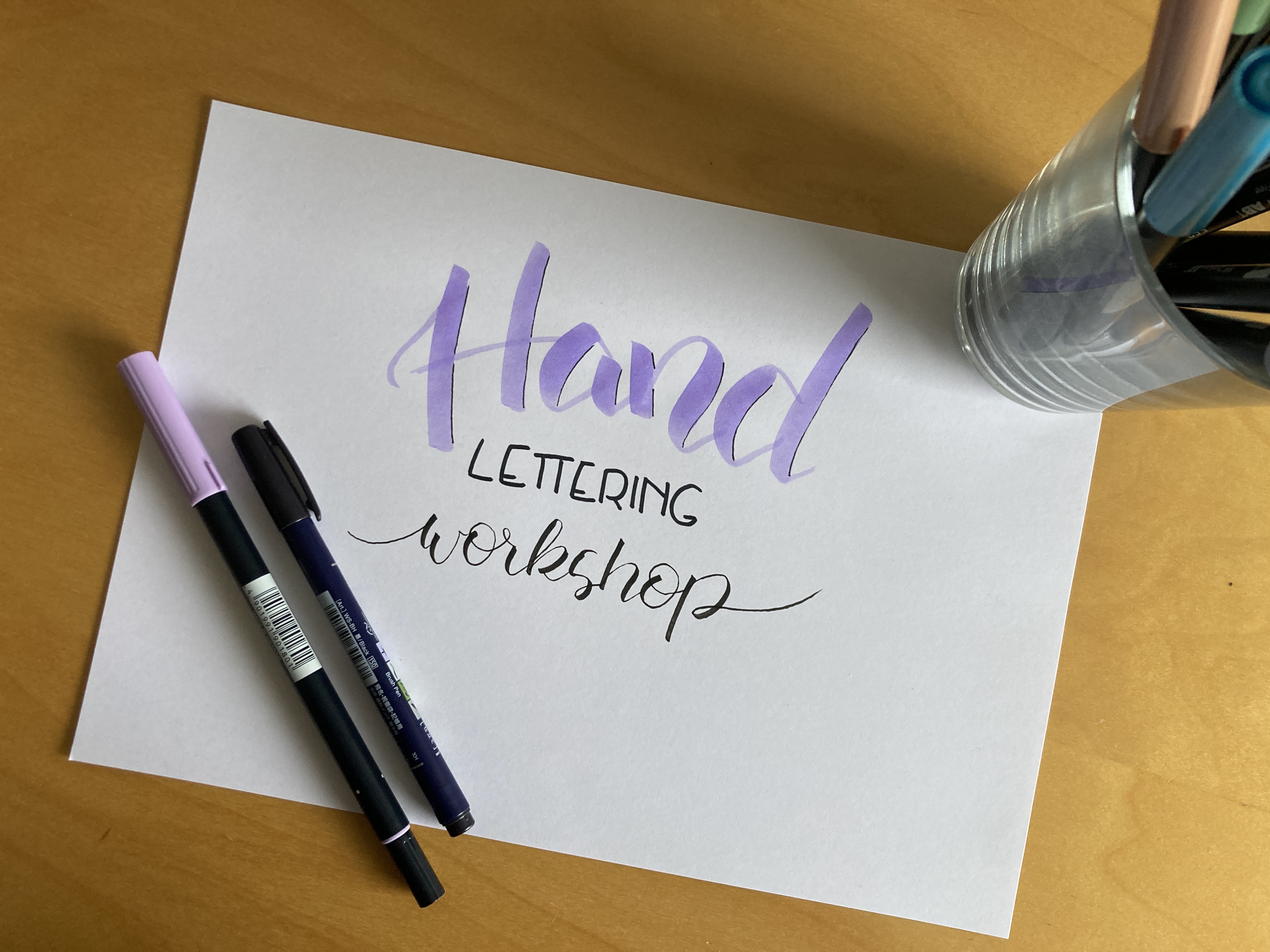 Handlettering Workshop auf Papier, umgeben von Stiften.