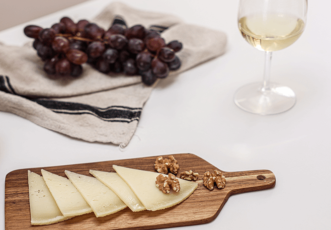 Cheese on a board surrounded by grapes and walnuts.