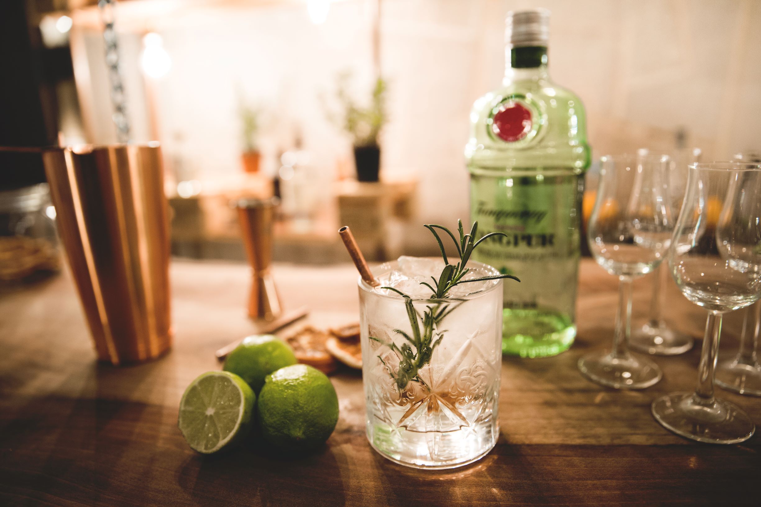 A cocktail glass with ice, limes and herbs on a table.