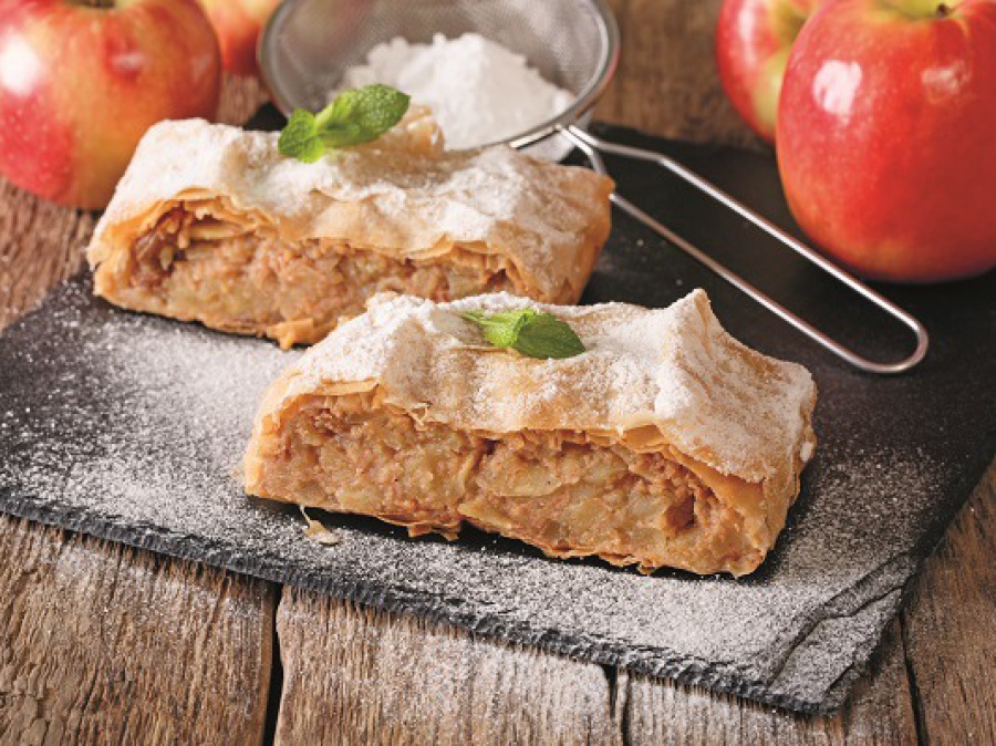 Apfelstrudel auf schwarzem Teller, mit Puderzucker bestreut.