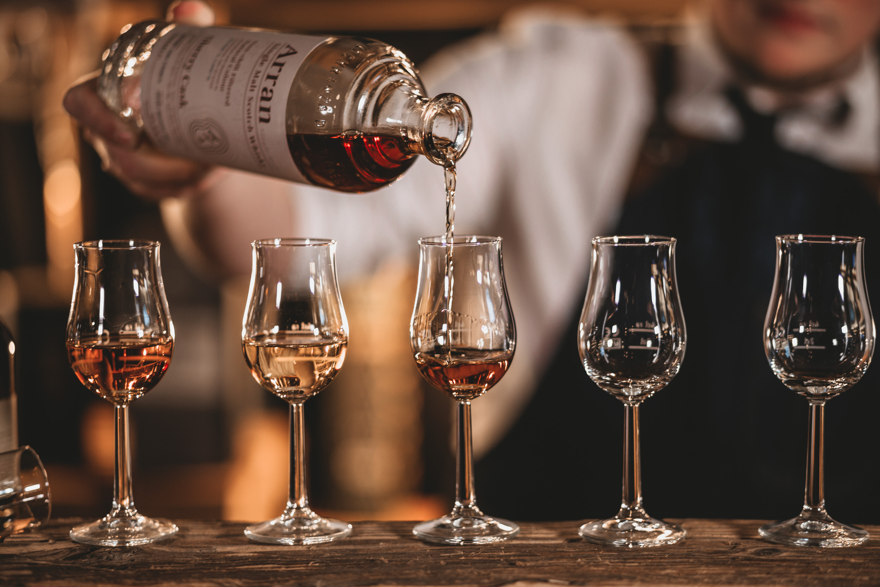 Ein Barkeeper schenkt Whisky in Gläser ein.