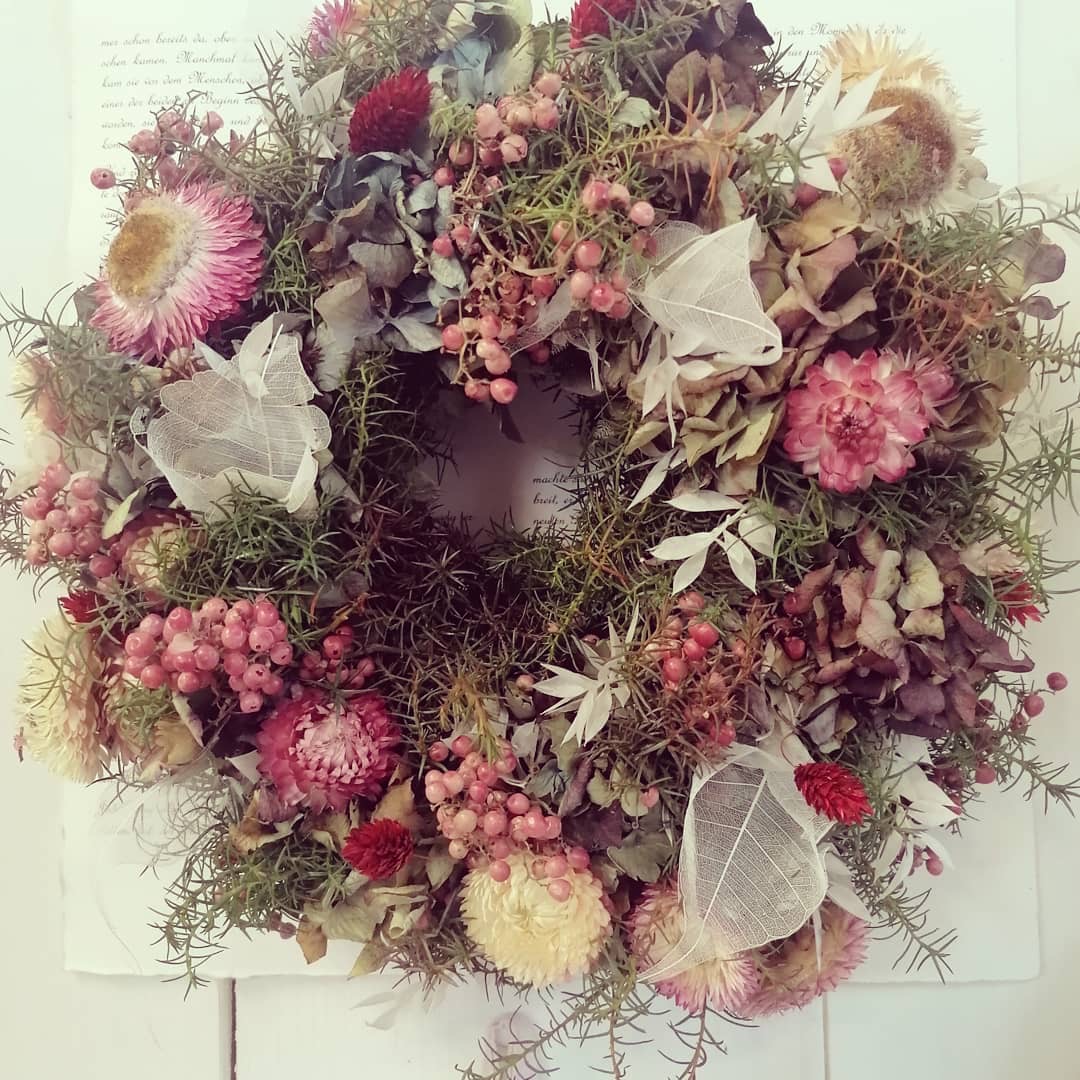 Blumenkranz hängt dekorativ, umgeben von Trockenblumen.