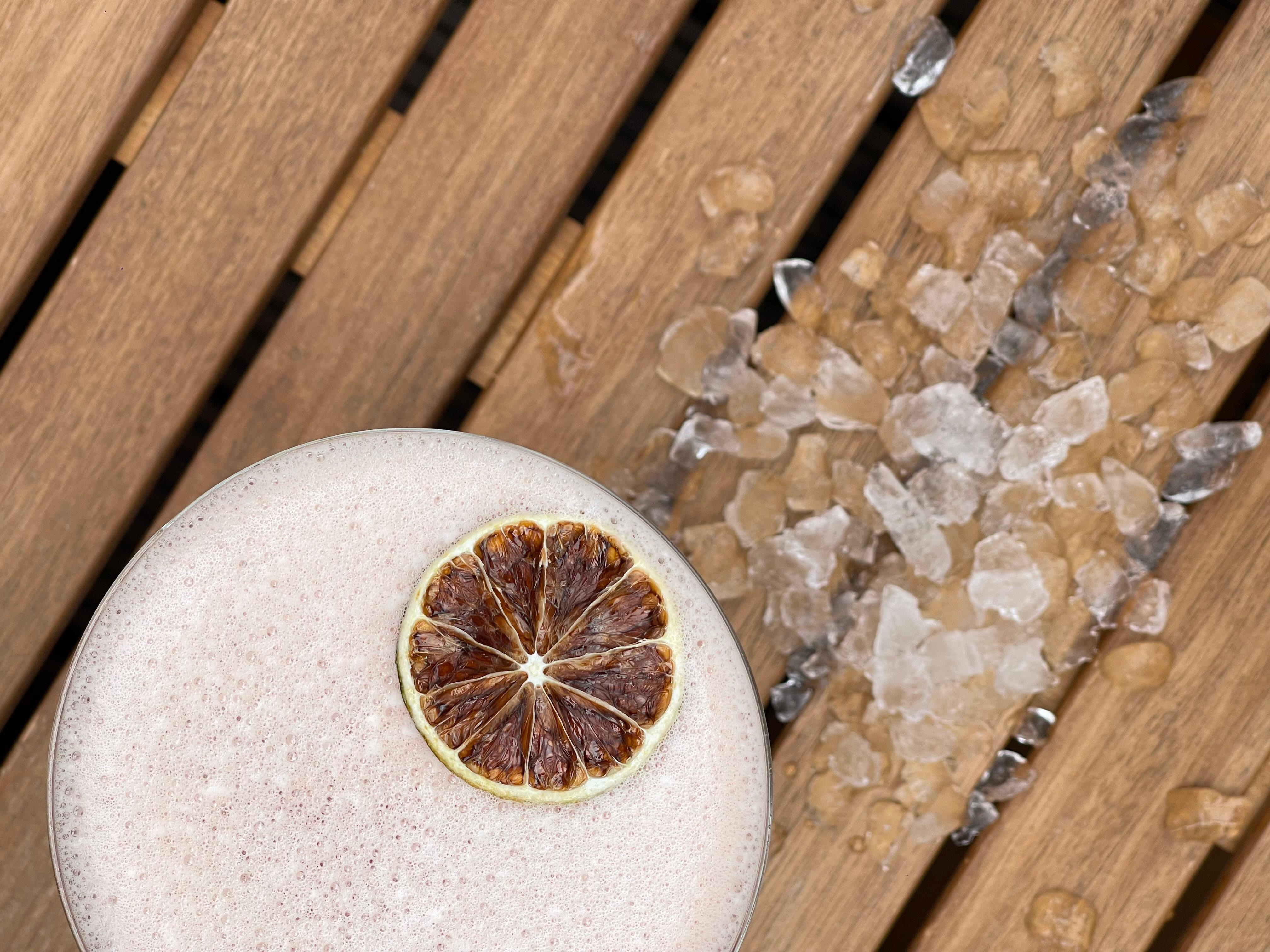Drink with dried lime is lying on a wooden surface next to ice.