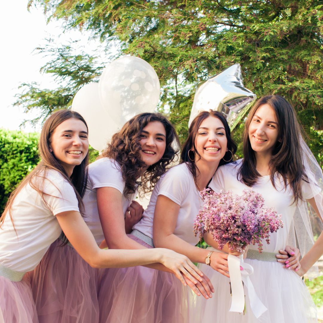Four women smile and pose with flowers and balloons.
