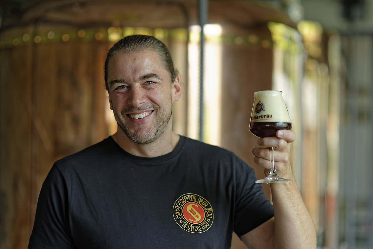 Man lifts a glass of beer in a brewery.