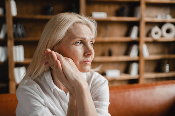 Woman sits thoughtfully in a bookshelf environment.