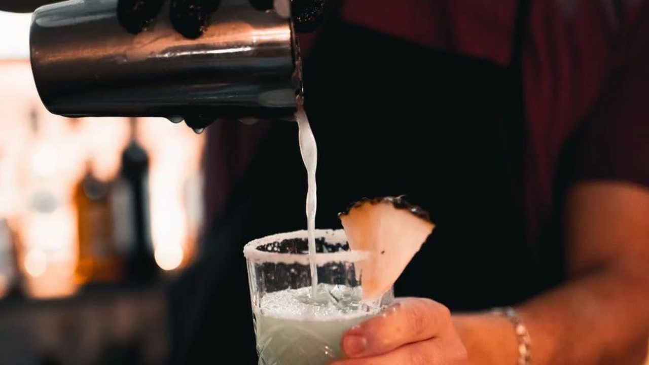Cocktail wird aus Shaker in Glas gegossen, fruchtig dekoriert.