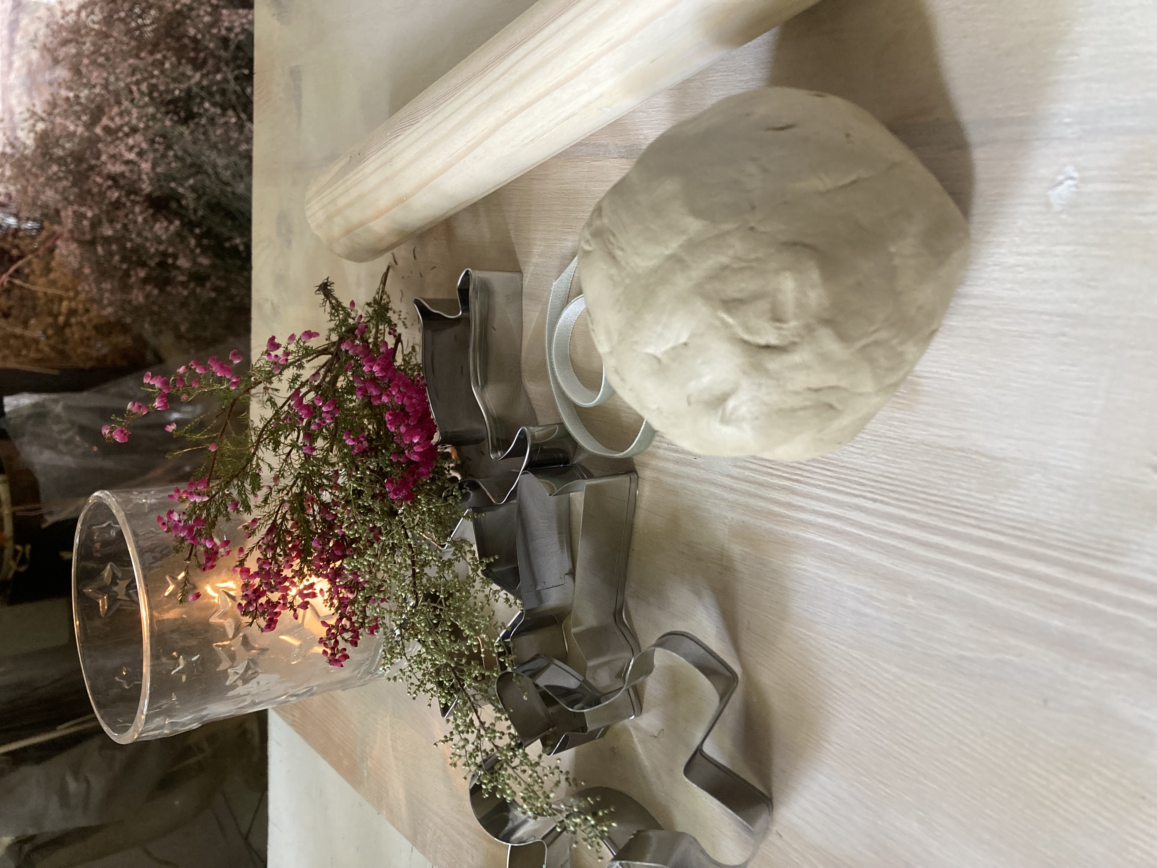 Cookie cutters, dough, rolling pin and flowers on table.