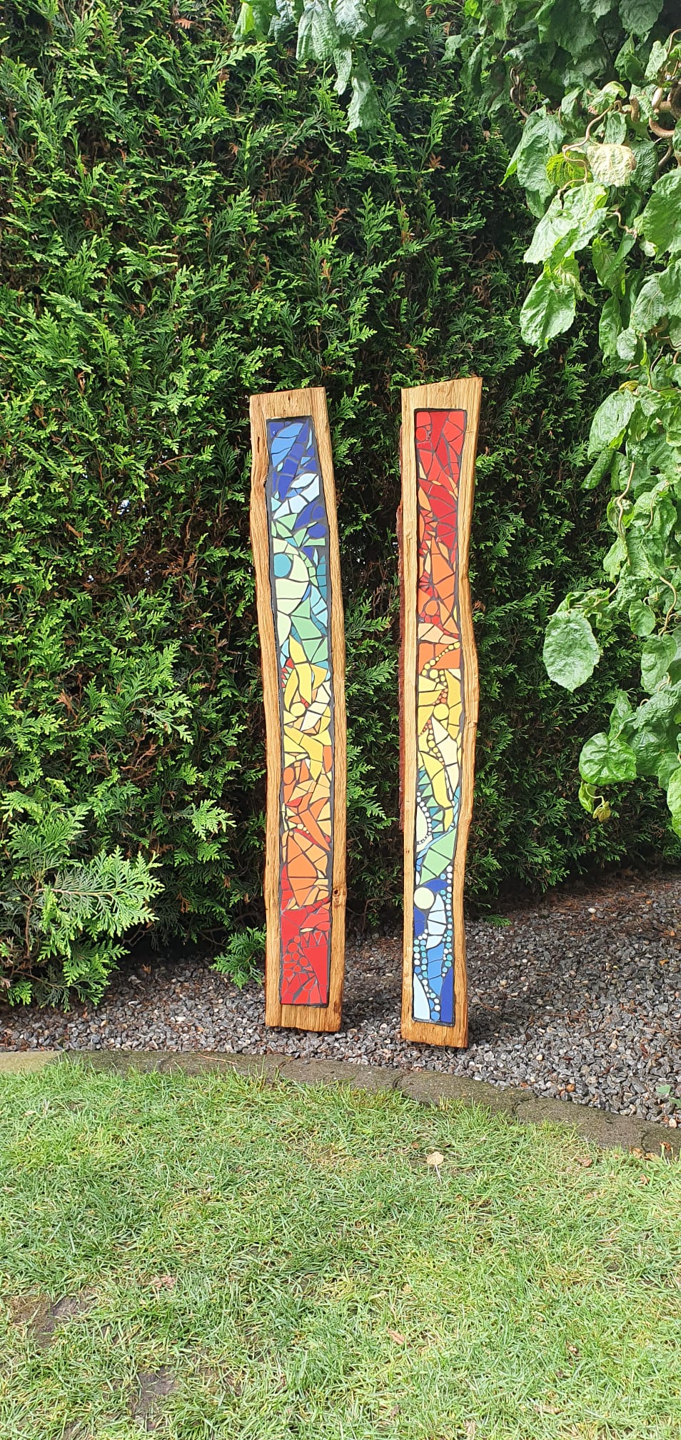 Colourful mosaic panels lie on wood, surrounded by plants.