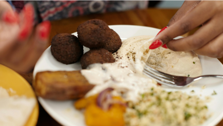 Hand scoops food on a plate with hummus, falafels, salad.