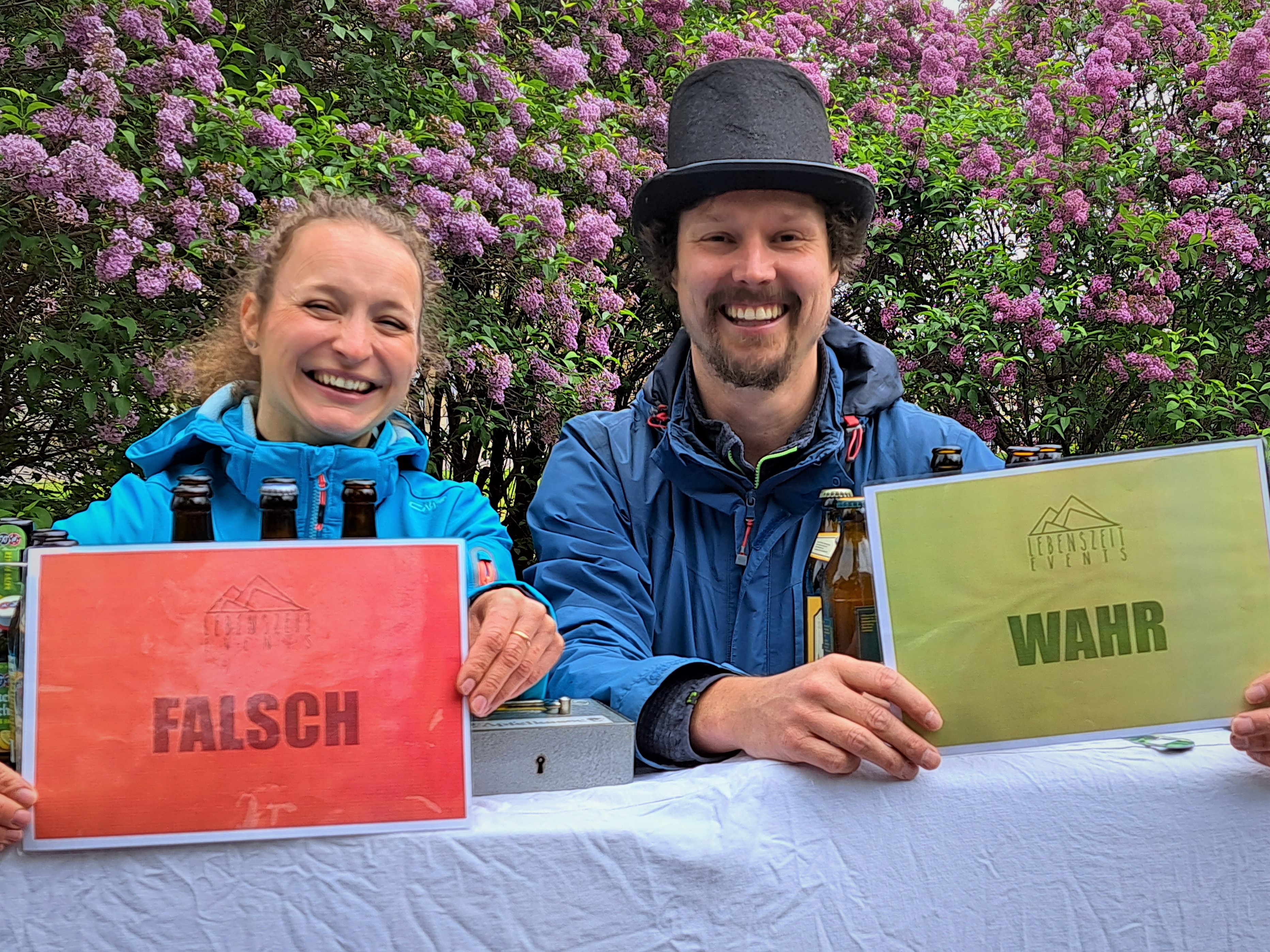 Zwei Personen draußen halten die Schilder „FALSCH“ und „WAHR“ hoch.