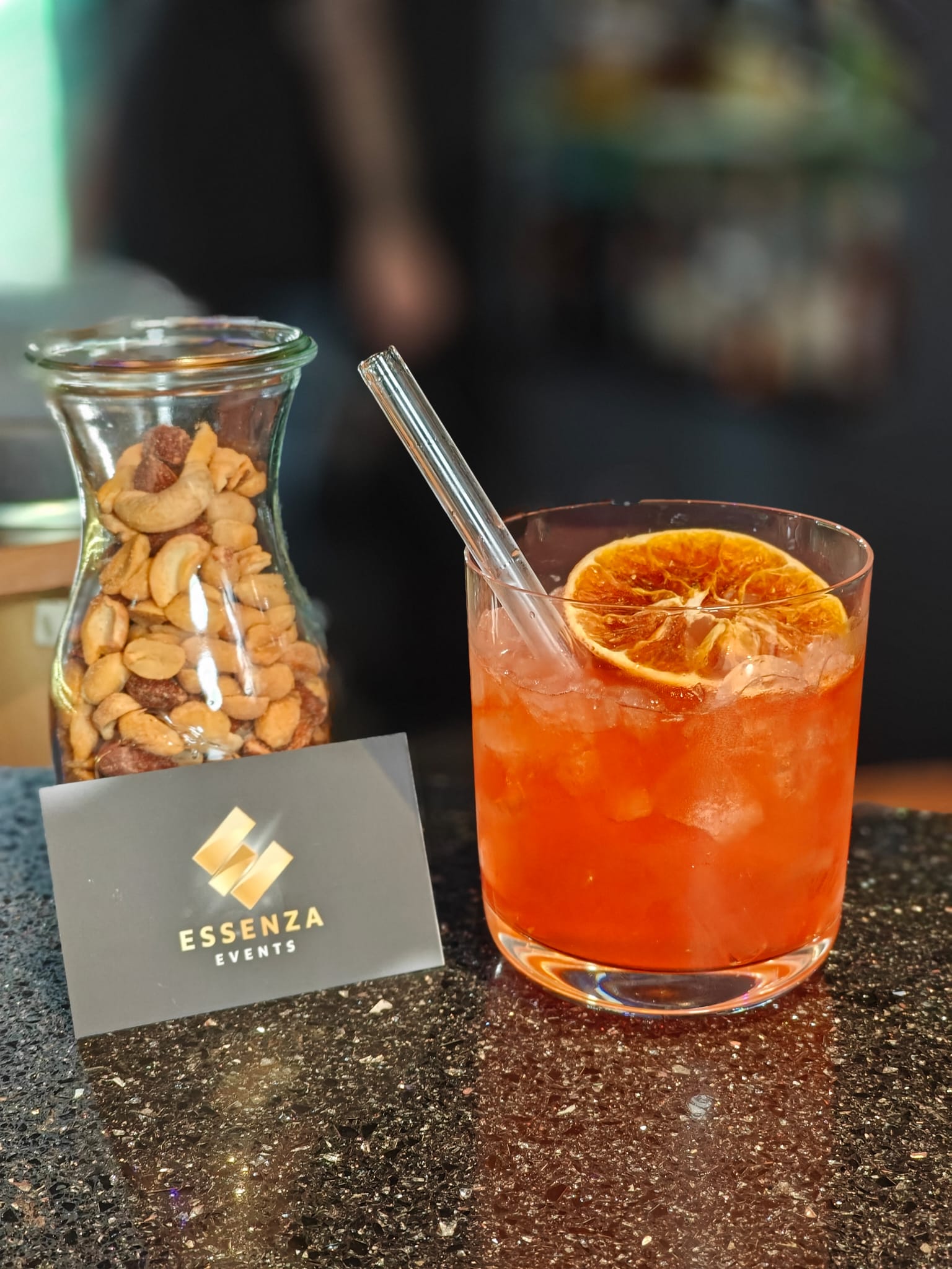 Orangencocktail mit getrockneten Zitrusscheiben und einem Glas mit gemischten Nüssen.