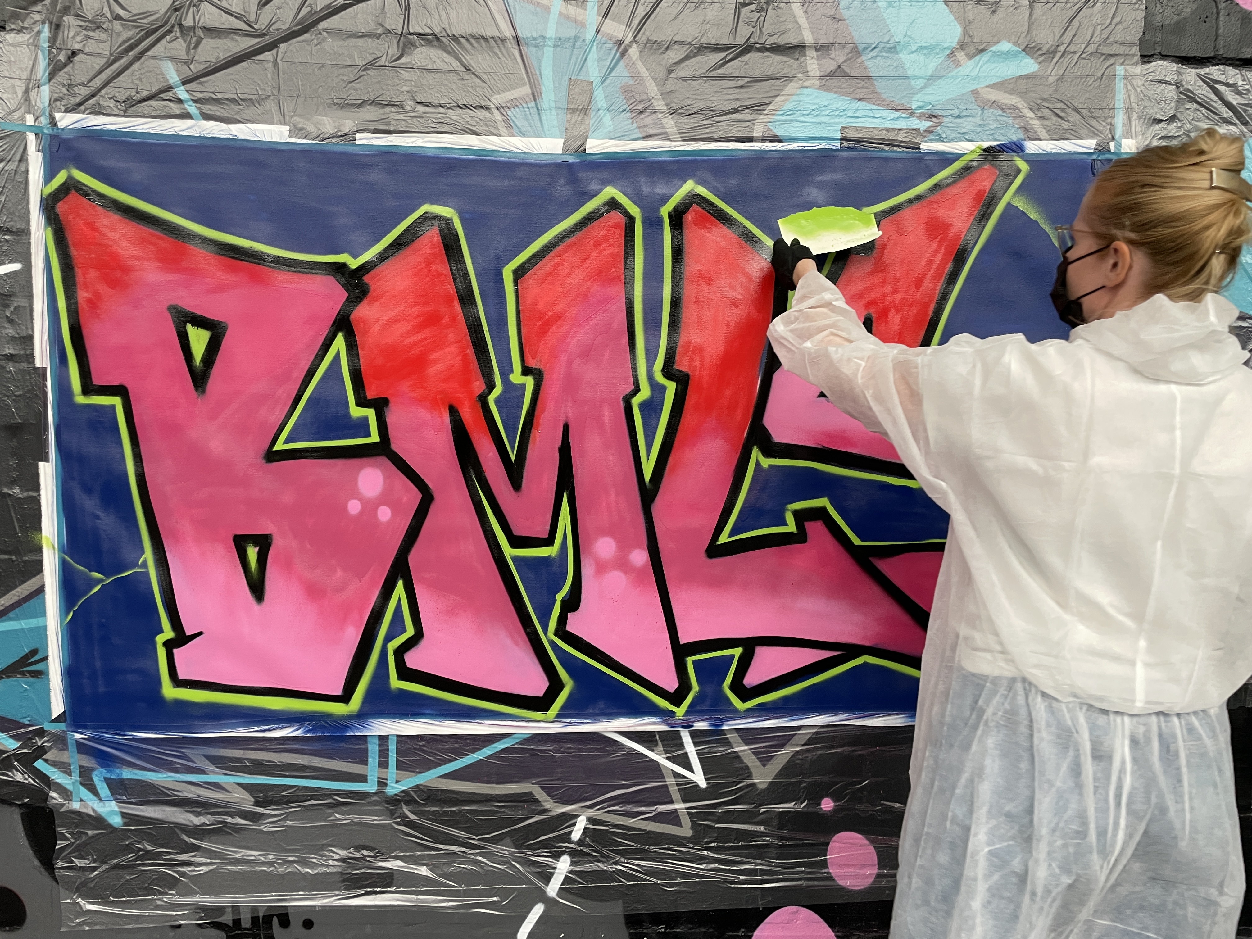 Artist painting graffiti letters on wall.