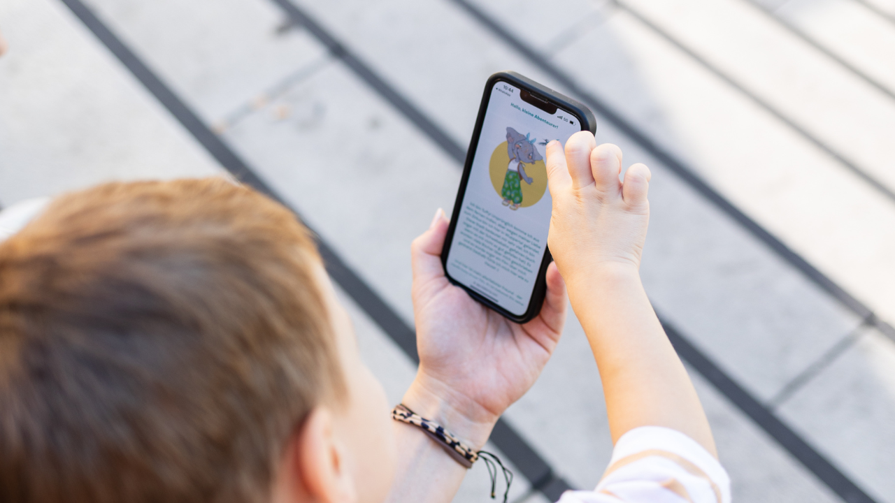 Child viewing cartoon on smartphone outdoors.