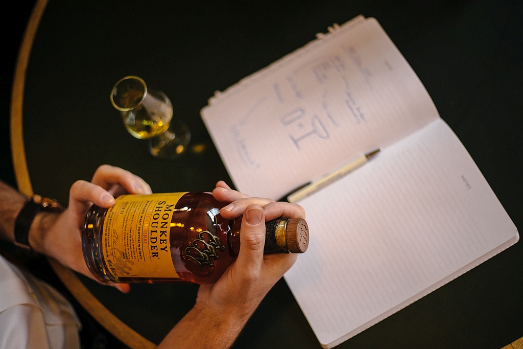 Person holding whiskey bottle near notebook.