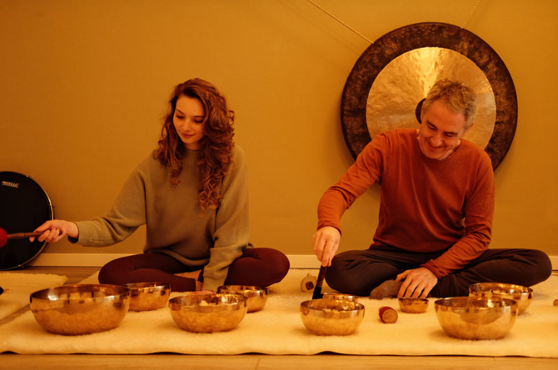Two people playing singing bowls indoors.