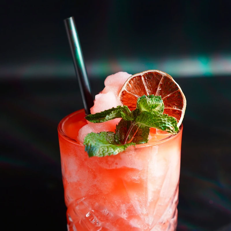 Red cocktail with mint, lime garnish.