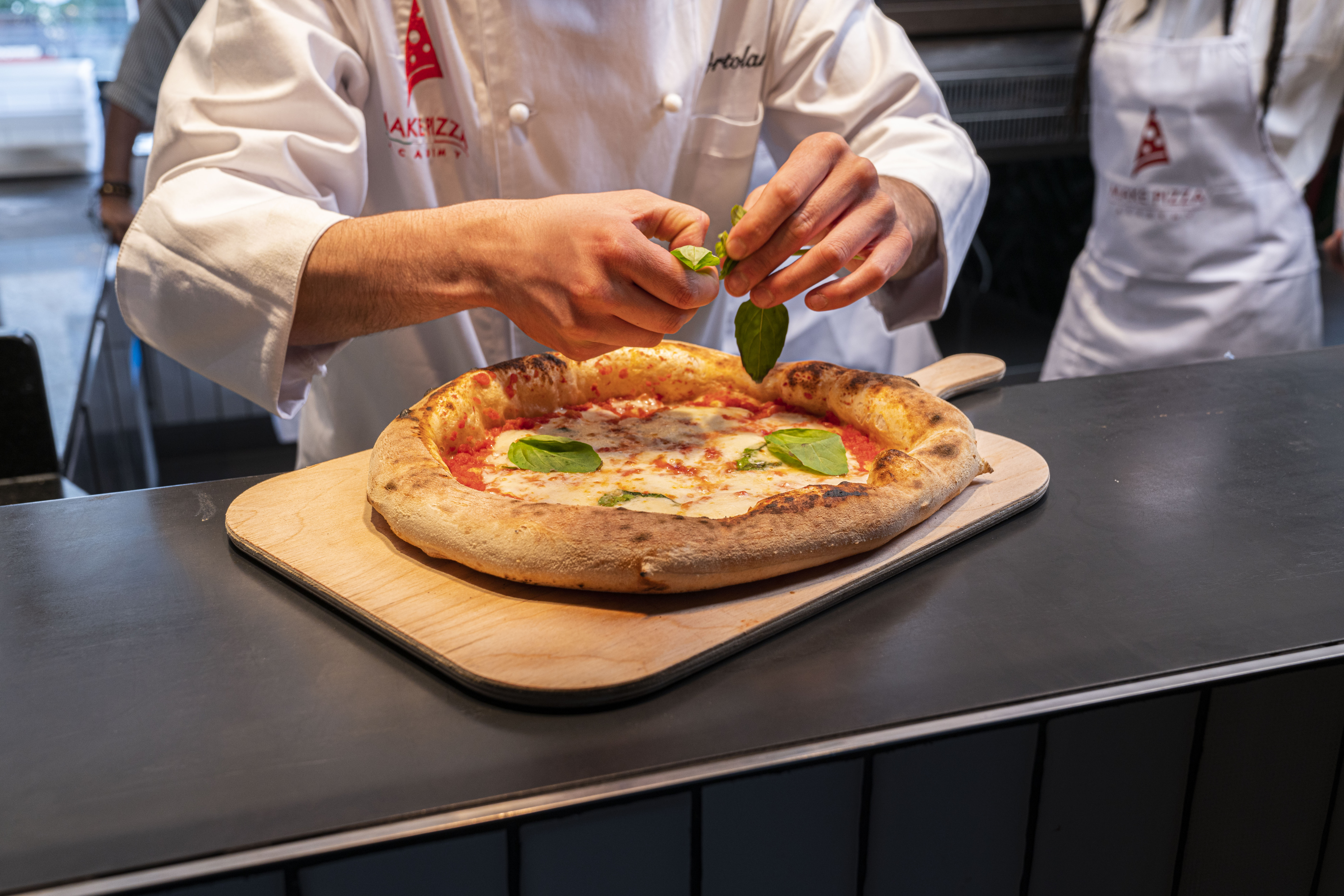 Koch legt Basilikum auf frisch gebackene Pizza.