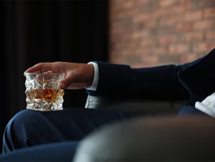 Person holding whiskey glass in relaxed setting.