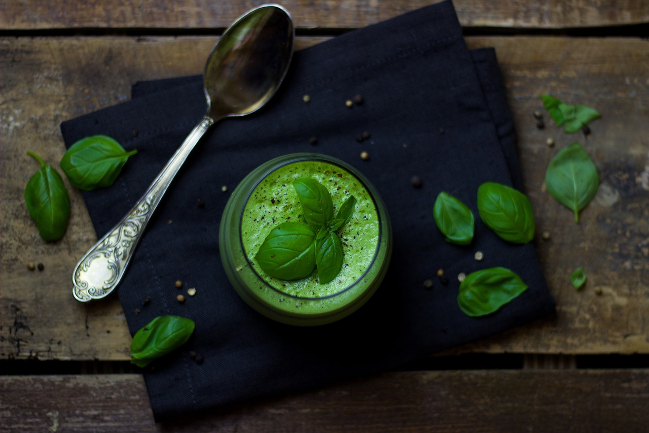 Green smoothie with basil leaves on table.