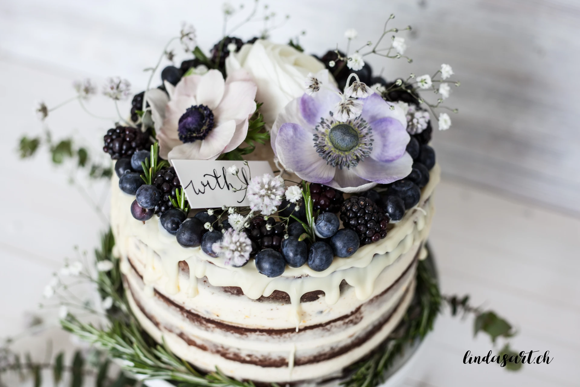 Naked cake with flowers and berries on top.