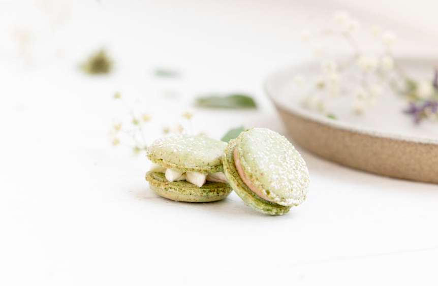 Green macarons on white surface with plate.