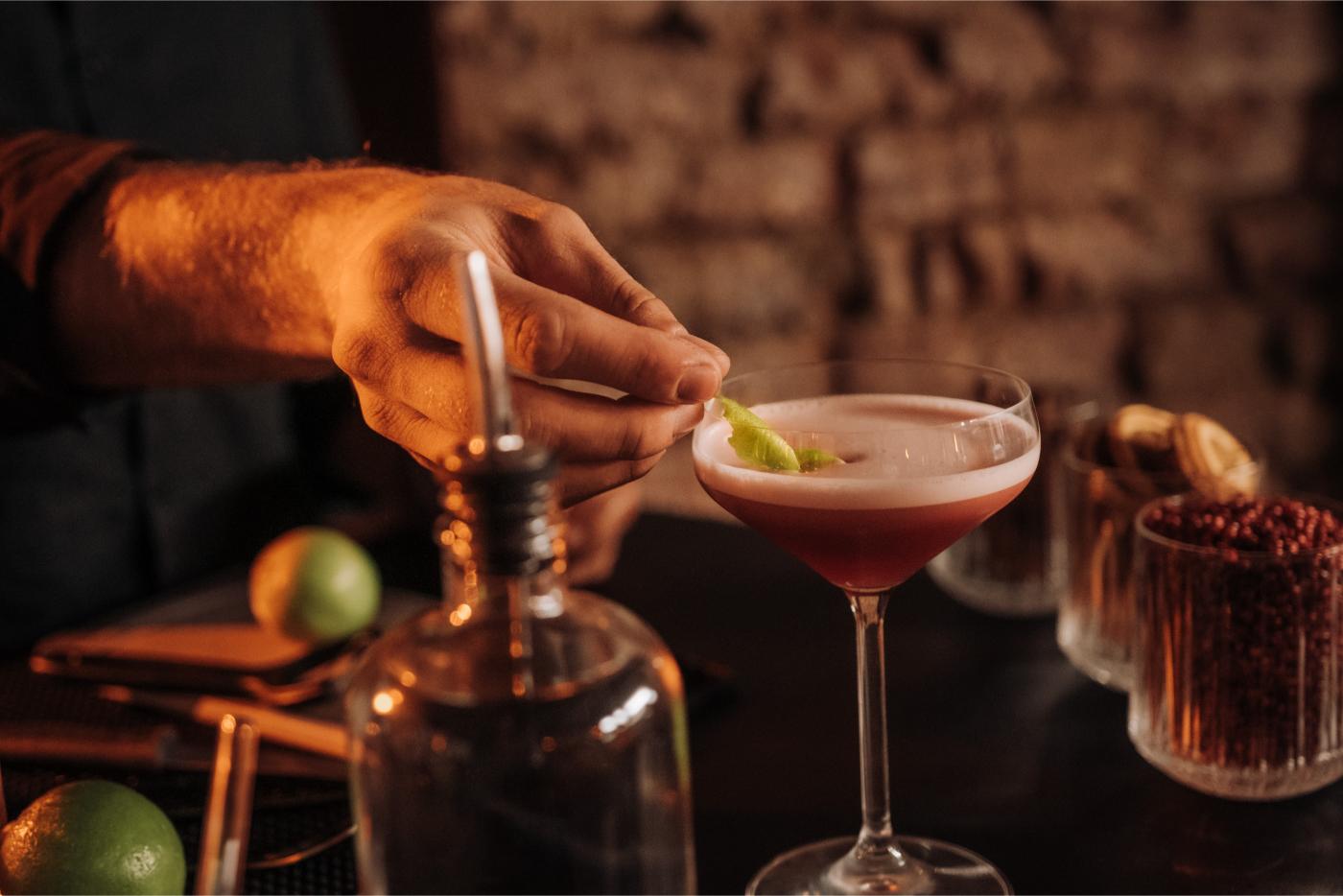 Hand garniert Cocktail mit Limette in dunkler Bar.