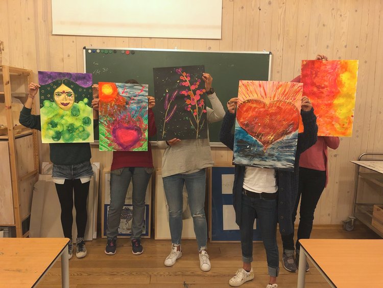 Personen halten bunte Gemälde im Klassenzimmer.