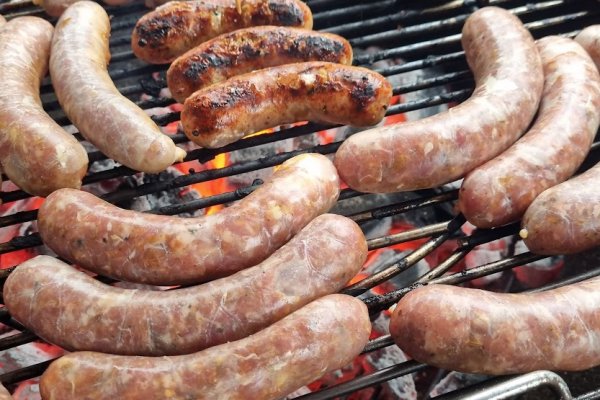 Sausages grilling over hot coals on barbecue.