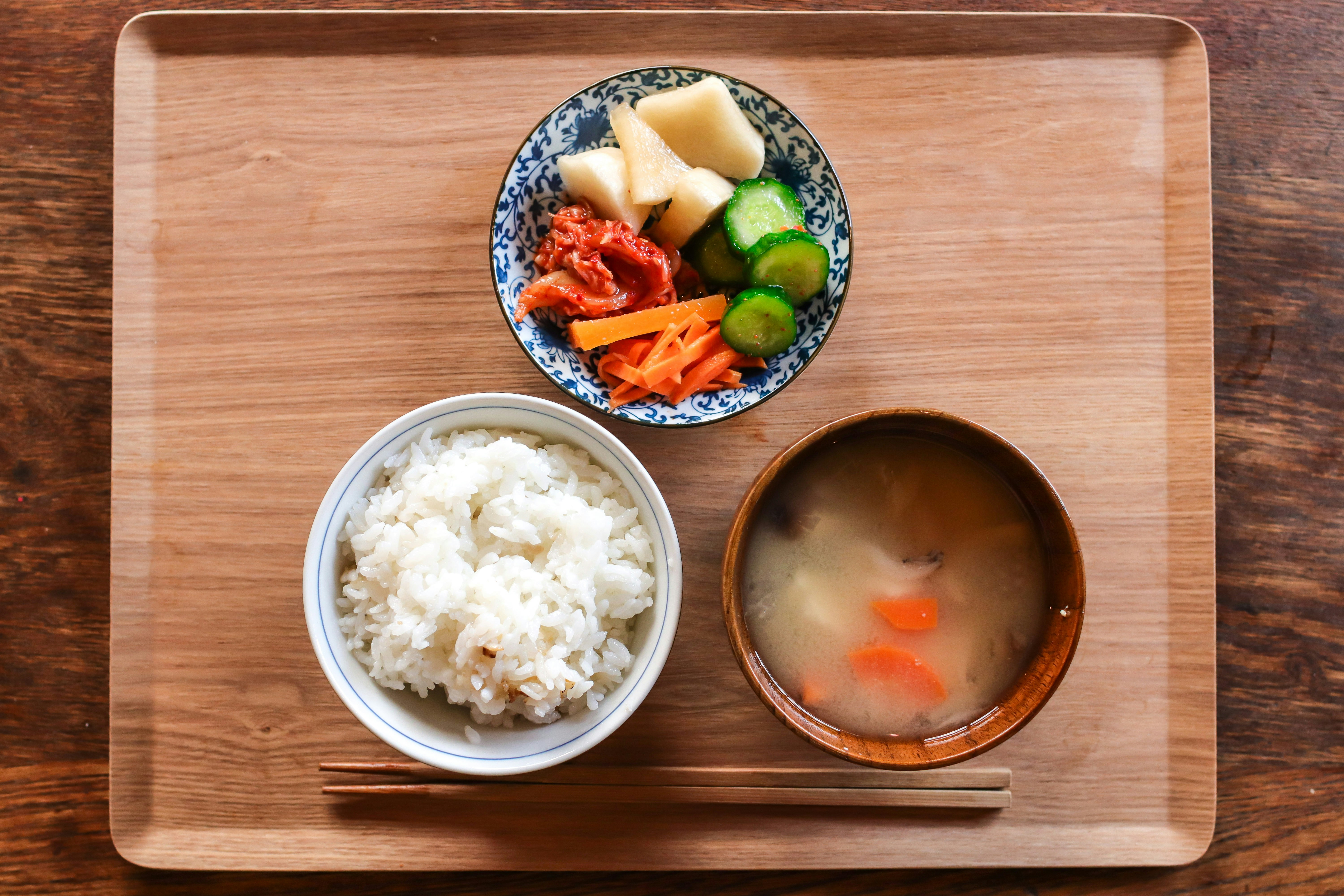 Rice, miso soup, and vegetables on wooden tray.