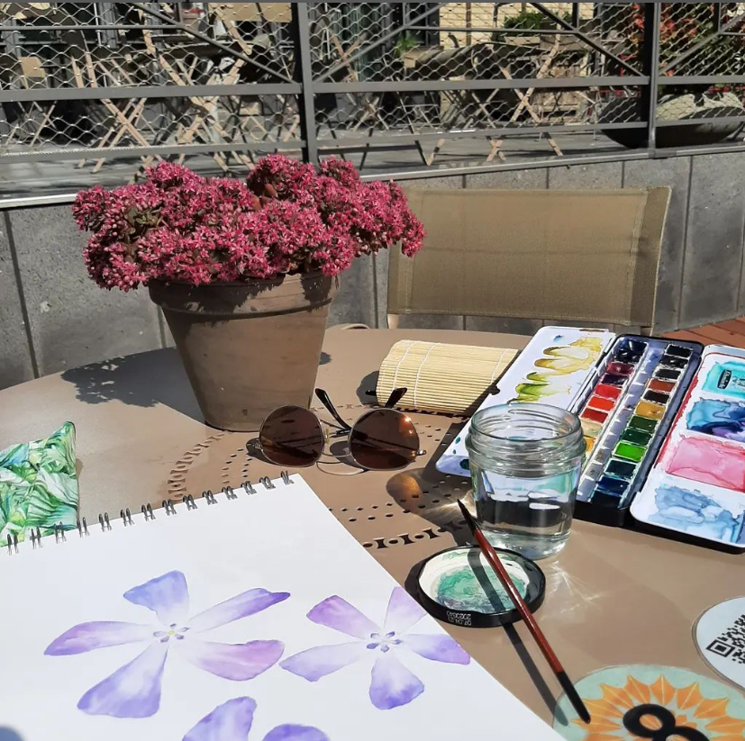 Aquarellpalette, Pinsel malt Blumenzeichnung am Tisch draußen.