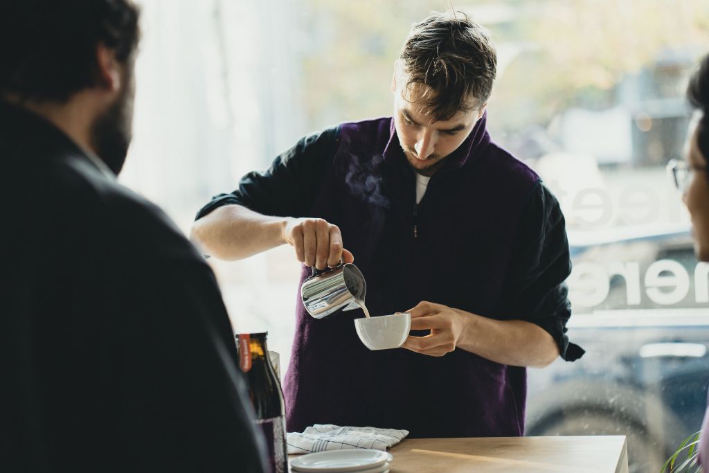 Person gießt Getränk in Tasse im Café.