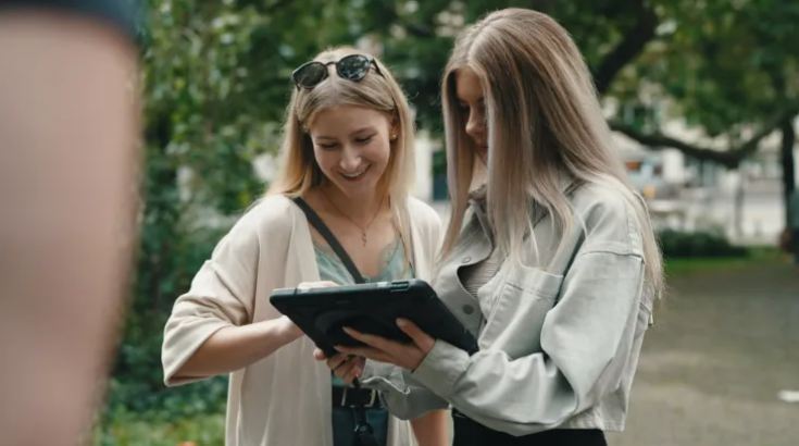 Zwei Frauen betrachten draußen ein Tablet.