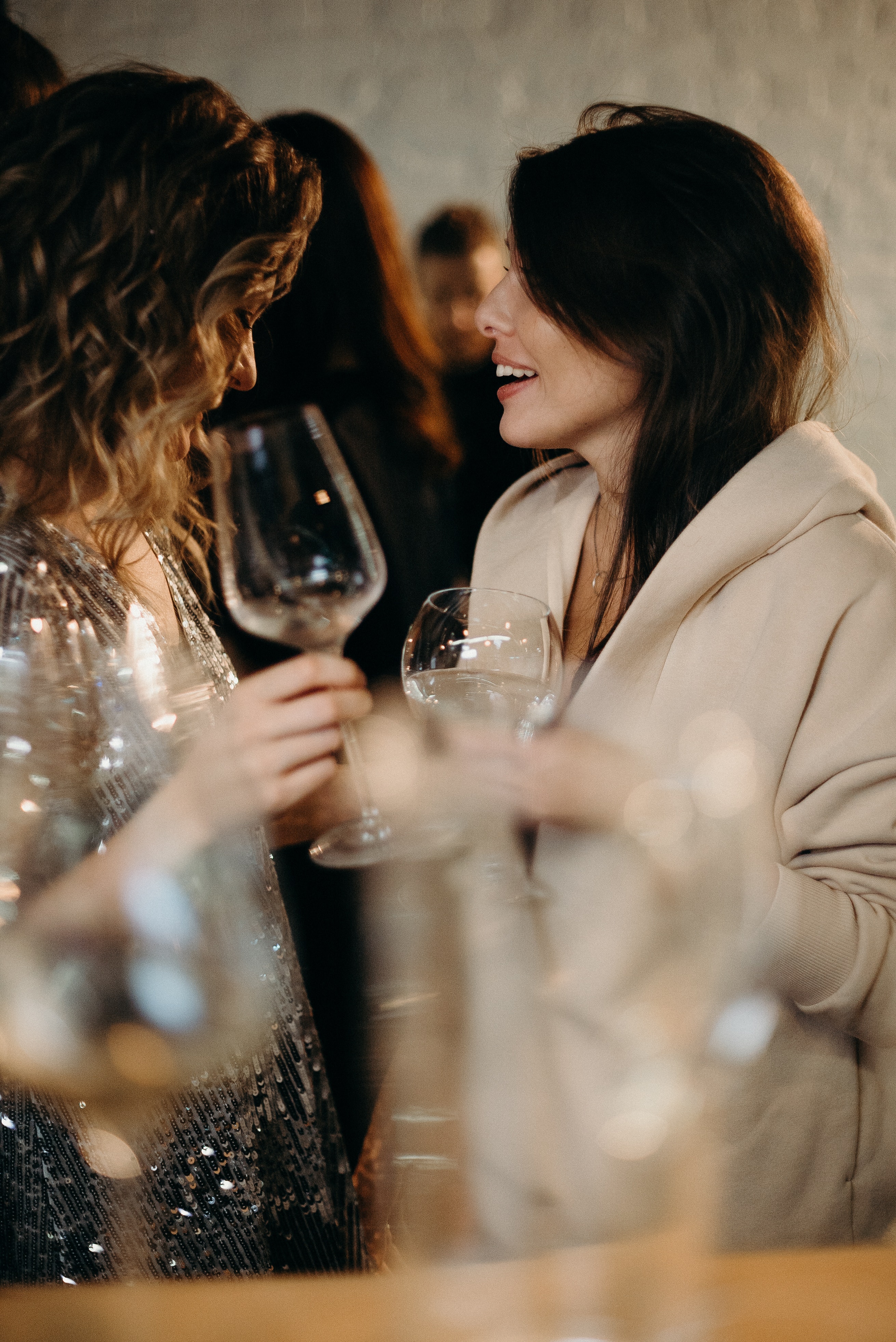 Two women are talking and holding wine glasses.