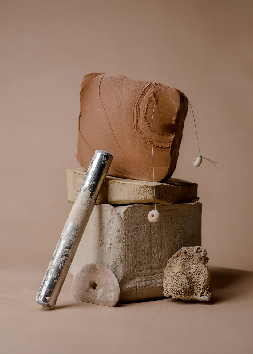 Abstract clay sculpture with metal tube against brown background.