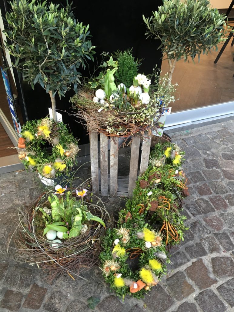 Wreaths and nest with plants on cobblestone ground.
