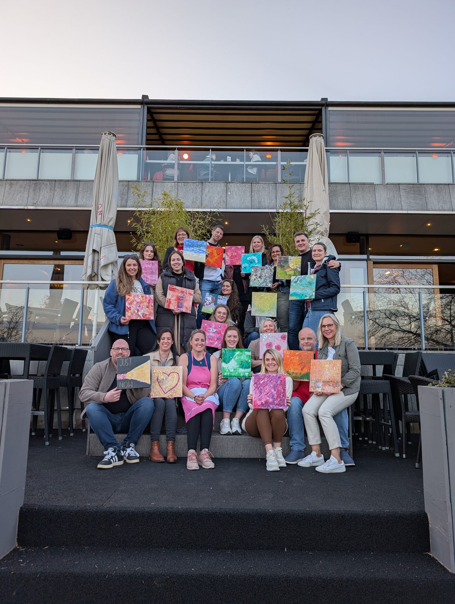Group of people holding colorful paintings outside.